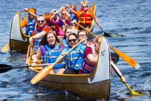 Two canoes being rowed by smiling people wearing lifejackets.