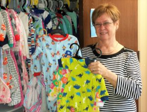 Carolyn Mills holding up a new pair of children's pajamas. In the background there are many more pajamas of different colors hanging in a closet