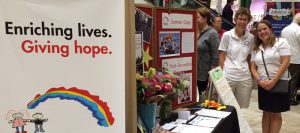 Two foundation members stand next to a KHCF booth at the Behind Closed Doors event.