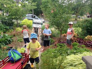 Four children standing outdoors near a sign that says Lettuce Stand.
