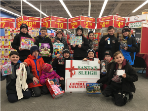 An image of a young boys' hockey team is shown standing around the KHCF Santa's Sleigh at Walmart, Chemong Road, Peterborough ON.  The boys hold cards with names and gift requests as well as the gifts they have purchased for donation to the KHCF Christmas Gift Giving Program.