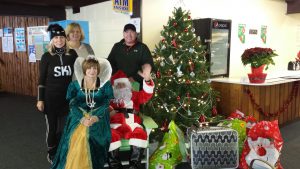 Four adults standing next to a Christmas tree and a person dressed as Santa.