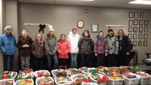 A group of children standing in front of a table covered with donated gifts for the Santa's Sleigh program.