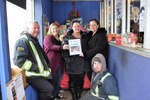 Five adults in a hallway. Three of them are holding up some kind of paper.