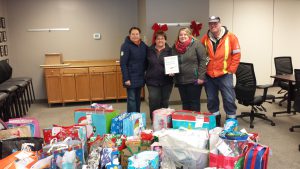 Four adults standing behind a pile of gifts donated to the Santa's Sleigh program.