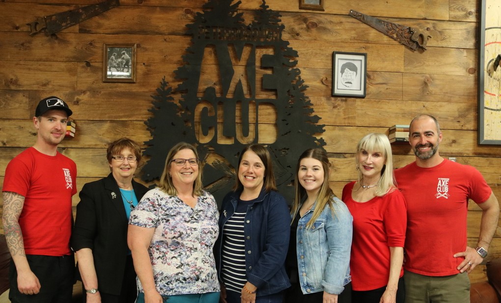 Seven adults standing in front of the Axe Club logo painted on the wall, inside the Axe Club building.