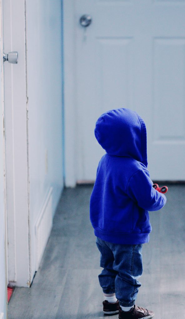 A small child in a blue hoodie stands with his back to the camera, holding a red fidget spinner.