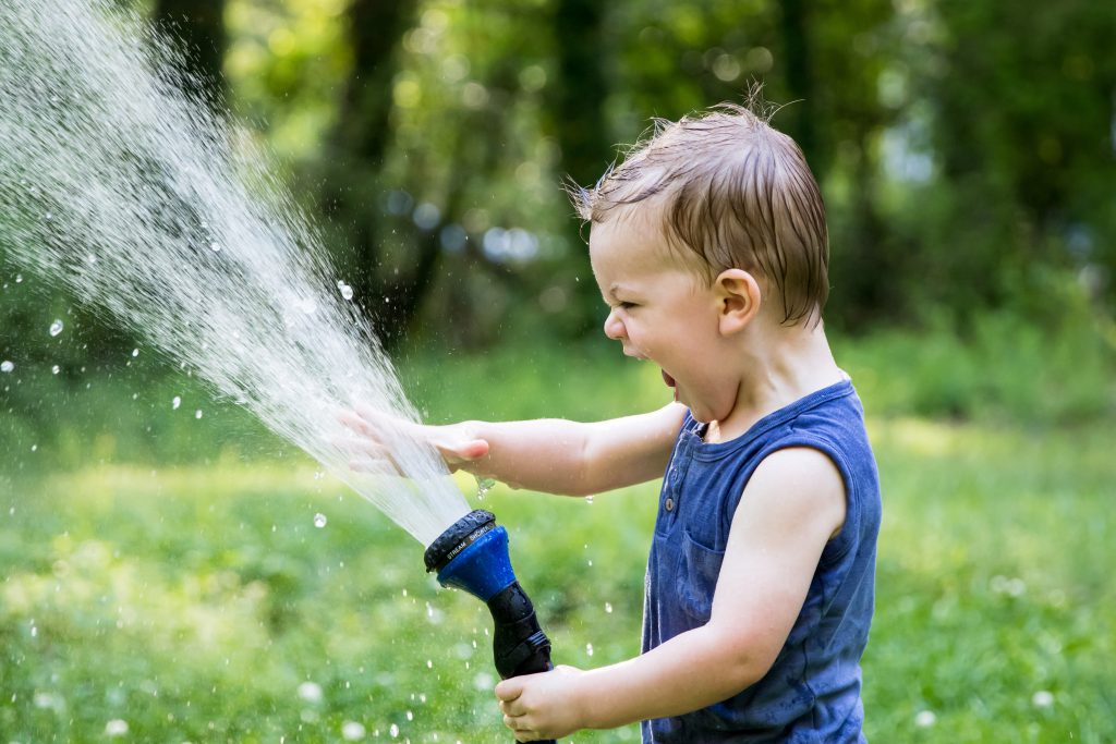 A little boy with his mouth open, holding a hose that is spraying water.