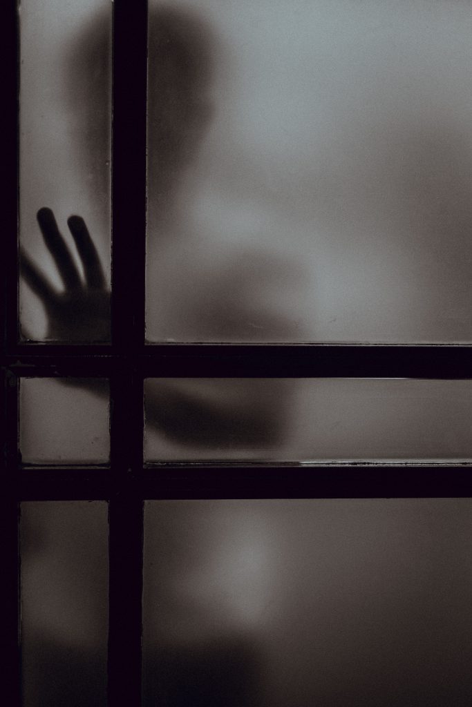 A child stands behind a foggy glass door, blurry except for their hand which is pressed against the glass.