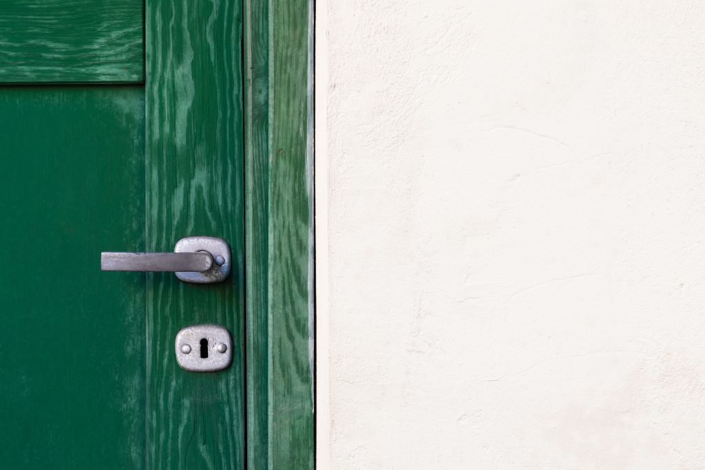 A close up of a green wooden door's metal handle.