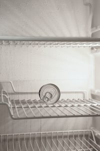 The inside of a barren fridge, containing only a single can lying on its side.