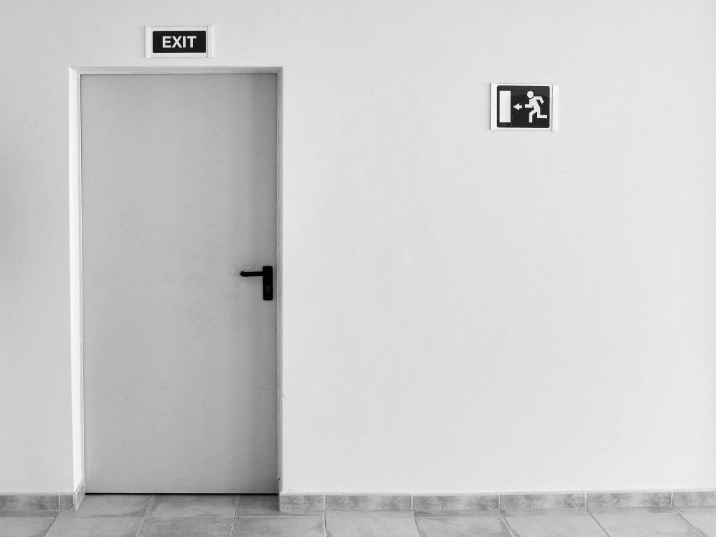 A white exit door in a white wall, with a black exit sign above it.