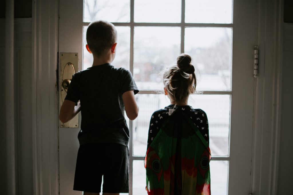 Two children standing in front of a glass door, looking outside.