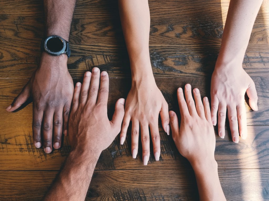 Five arms of varying skin tones rest on a table next to each other, palms down.