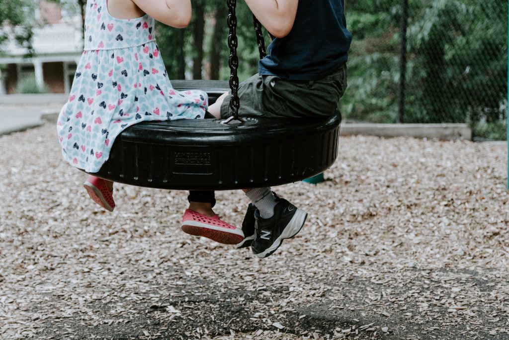 Two kids sit on a tire swing, only visible from the neck down.
