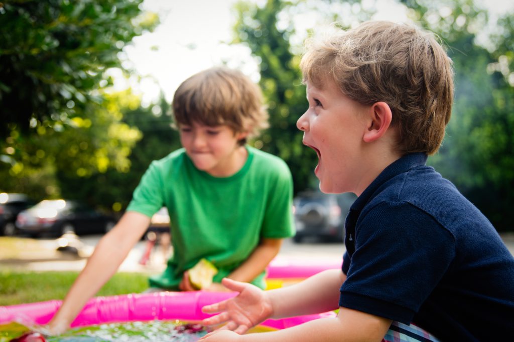 Two young boys playing outdoors; one of them has an expression of joy.