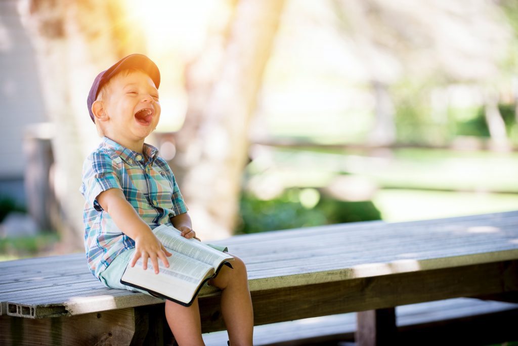 A child sitting on a bench and laughing, with a large open book on his lap.