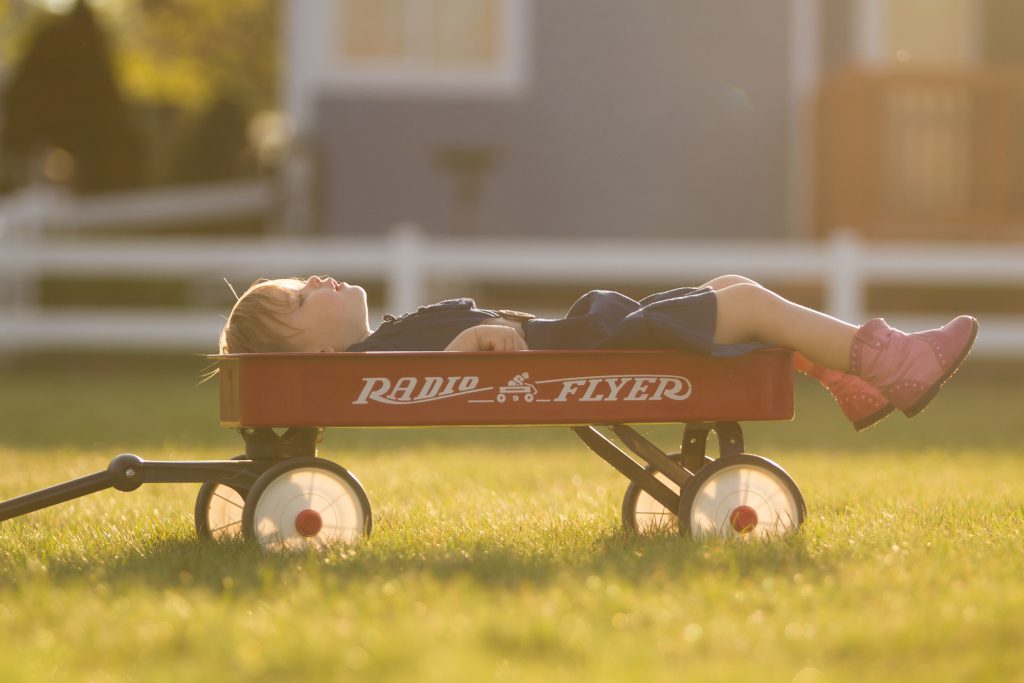 A child lying down in a red wagon outdoors.