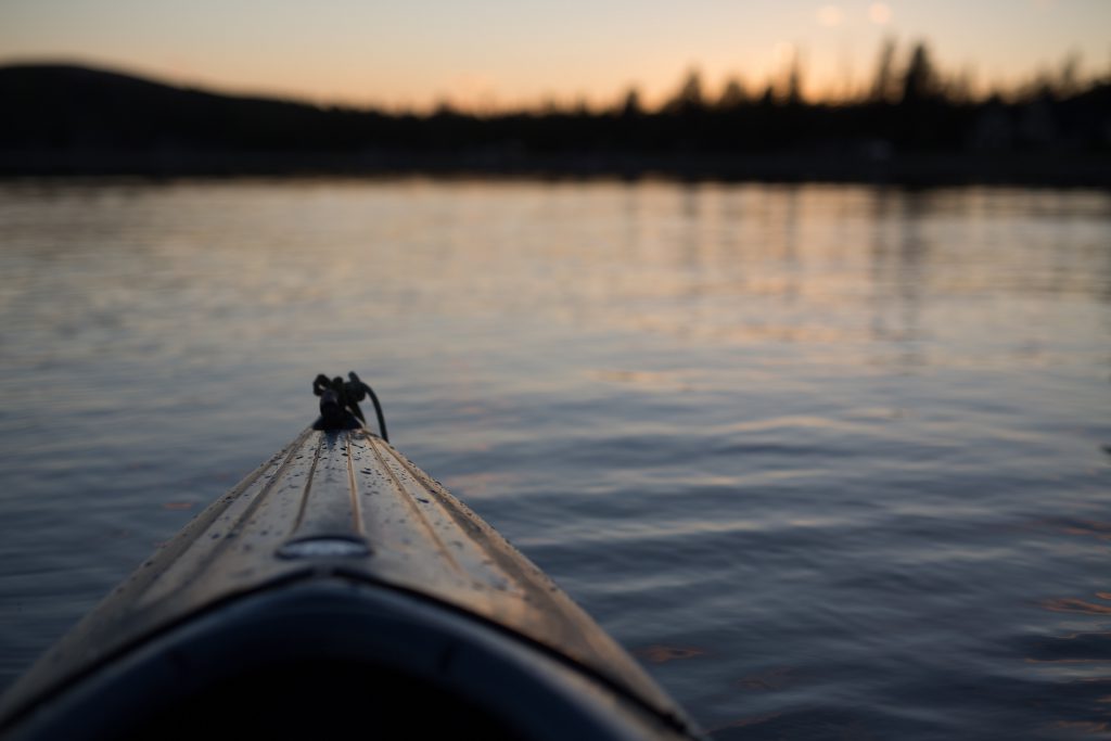 The tip of a canoe is visible as it floats on a lake, as the sun sets.
