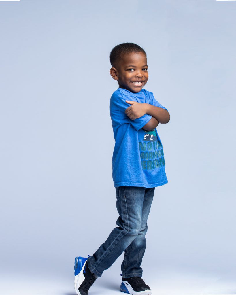 A little boy wearing a blue shirt smiles at the camera.