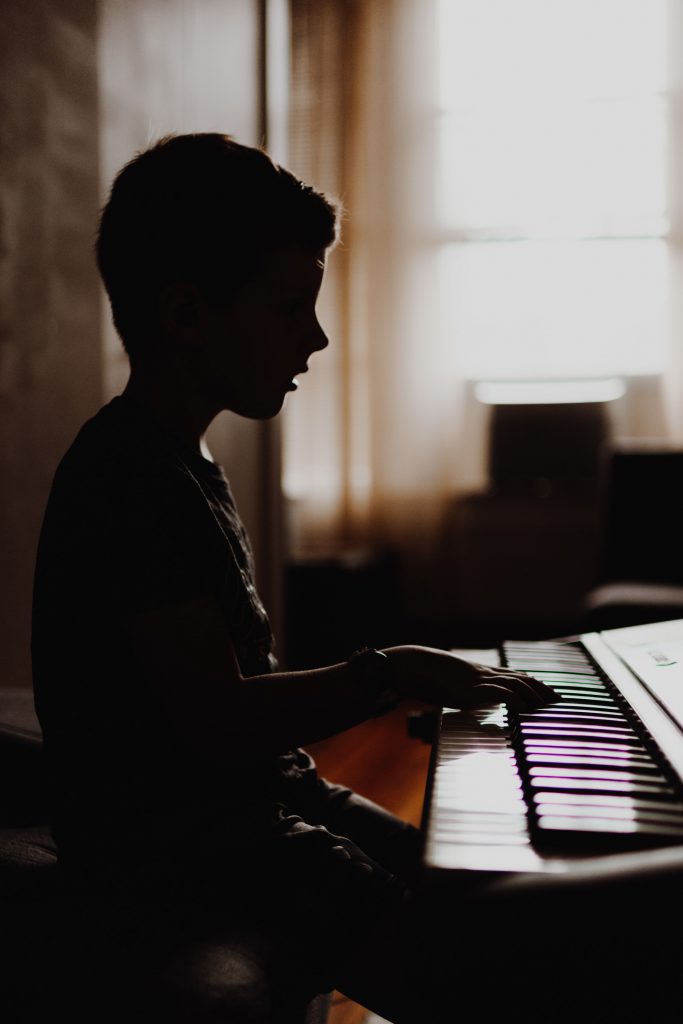 A dimly lit image of a child sitting at a piano.
