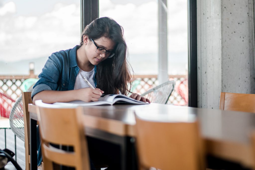 A teen sitting at a table, studying from a book.