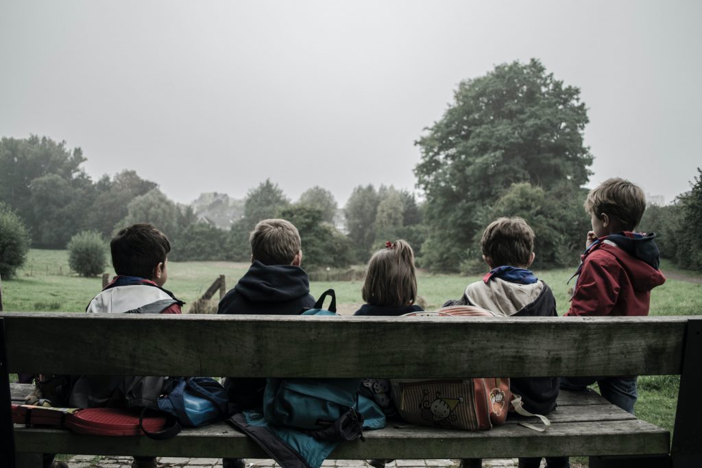 Five children sitting on a wooden bench outdoors.