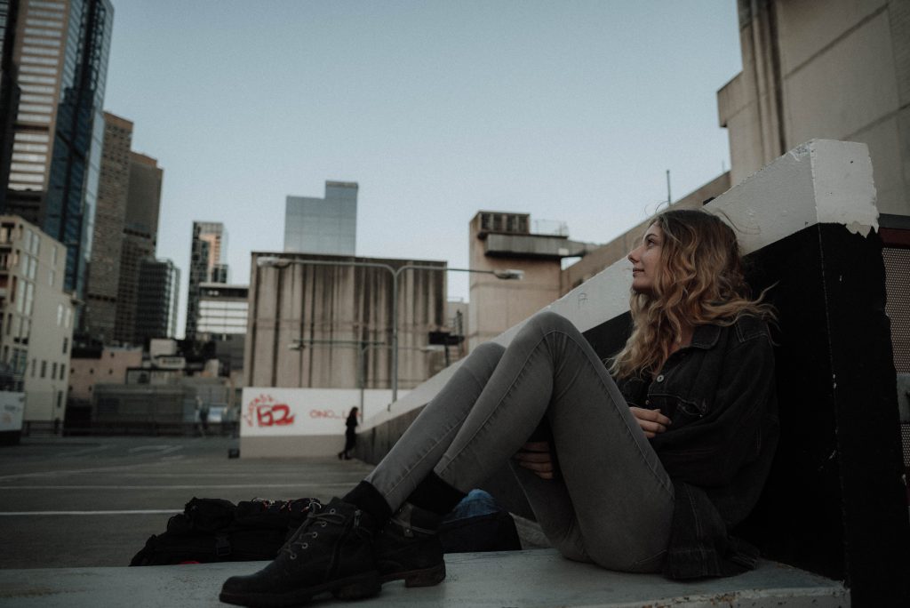 A teen in a city, sitting against a wall.