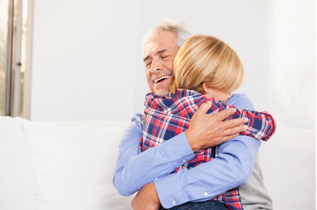 A child and their grandparent hugging each other in a white room.