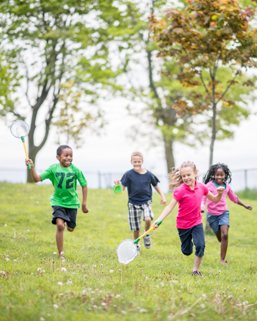 Four kids running in a field, two of them holding butterfly nets.