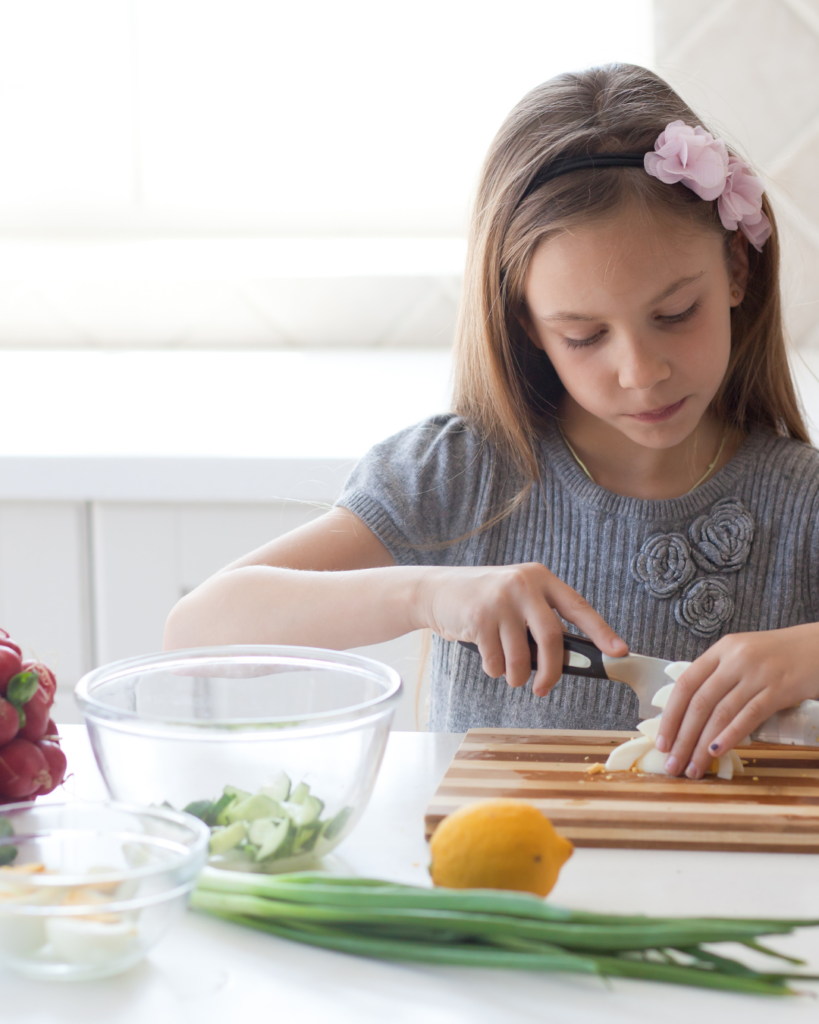 A young person in a kitchen, chopping a vegetable.