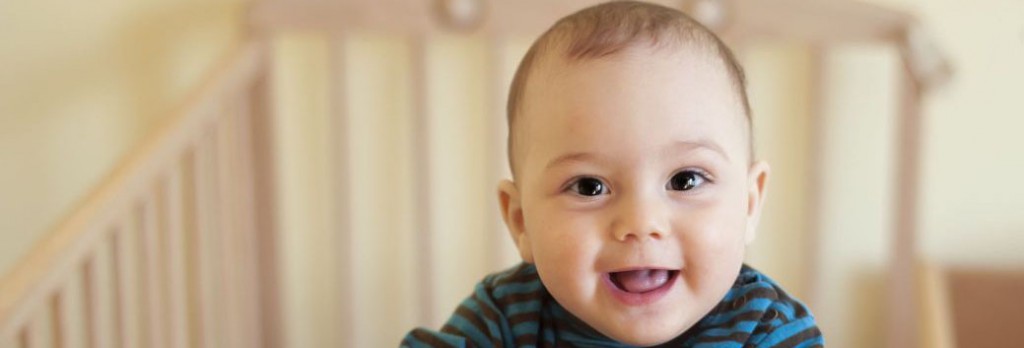 Baby with a cute happy face standing in a cot.
