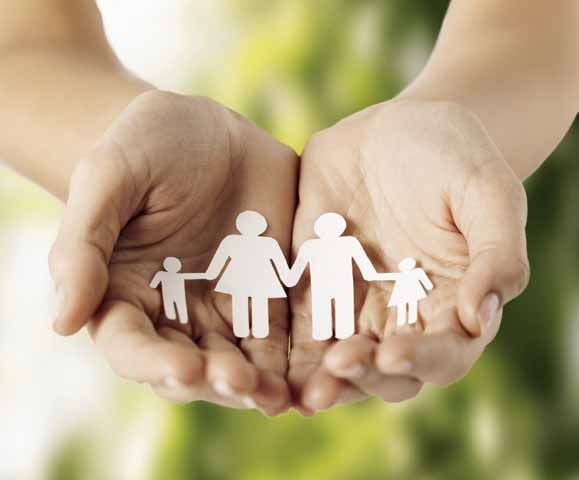 multicultural hands supporting a paper cutout of a family featuring two parents and two children